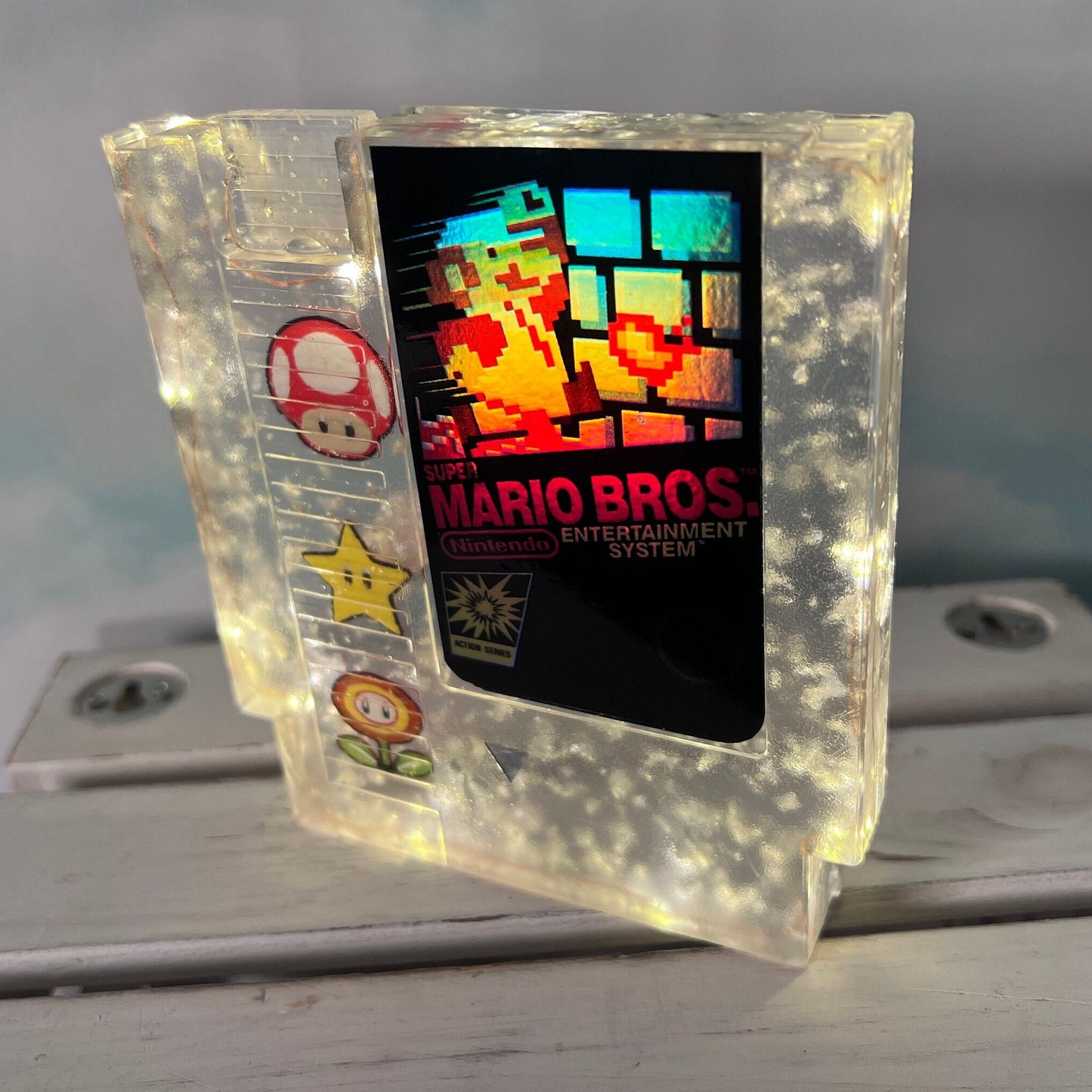 Handmade resin art featuring a retro Super Mario Bros NES cartridge with classic icons like the mushroom, fire flower, and star. Perfect for gamers, collectors, or unique home decor to add a nostalgic touch to any space.