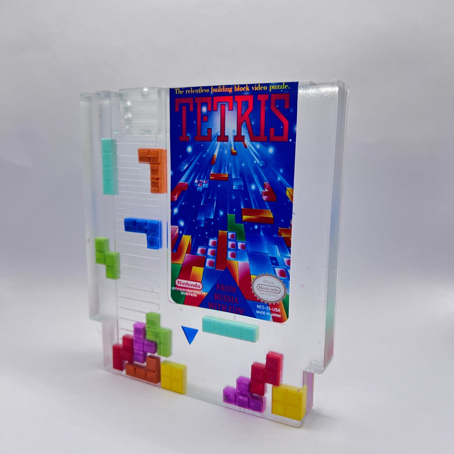 Clear resin NES cartridge art featuring vibrant 3D Tetris block embellishments for a unique retro gaming display. This handmade decorative item is a must-have for gaming enthusiasts and collectors of Nintendo memorabilia.