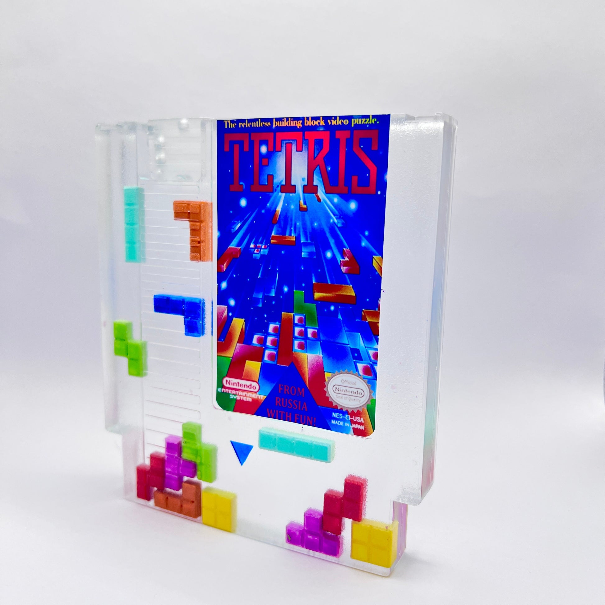 Clear resin NES cartridge art featuring vibrant 3D Tetris block embellishments for a unique retro gaming display. This handmade decorative item is a must-have for gaming enthusiasts and collectors of Nintendo memorabilia.