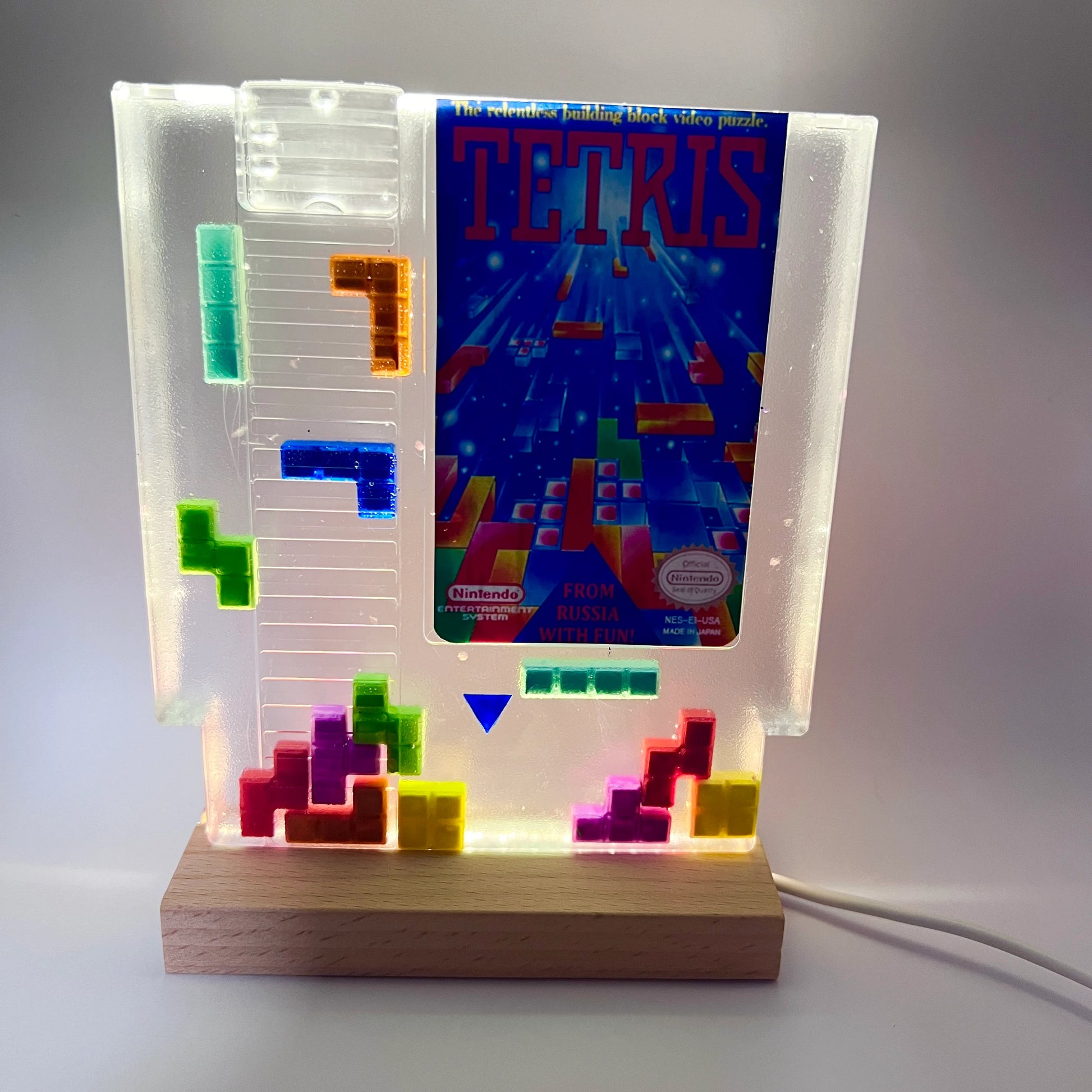 Clear resin NES cartridge art featuring vibrant 3D Tetris block embellishments for a unique retro gaming display. This handmade decorative item is a must-have for gaming enthusiasts and collectors of Nintendo memorabilia.