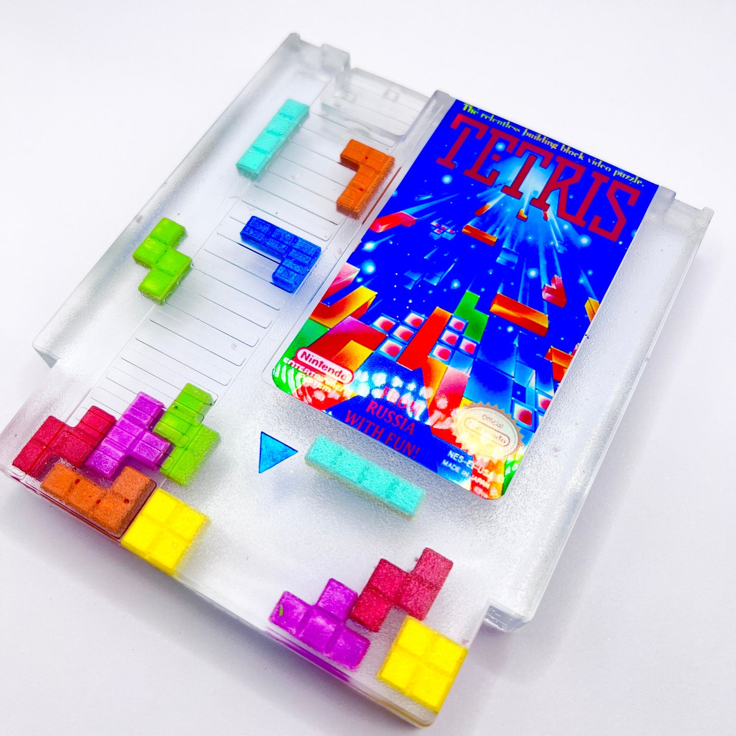 Clear resin NES cartridge art featuring vibrant 3D Tetris block embellishments for a unique retro gaming display. This handmade decorative item is a must-have for gaming enthusiasts and collectors of Nintendo memorabilia.