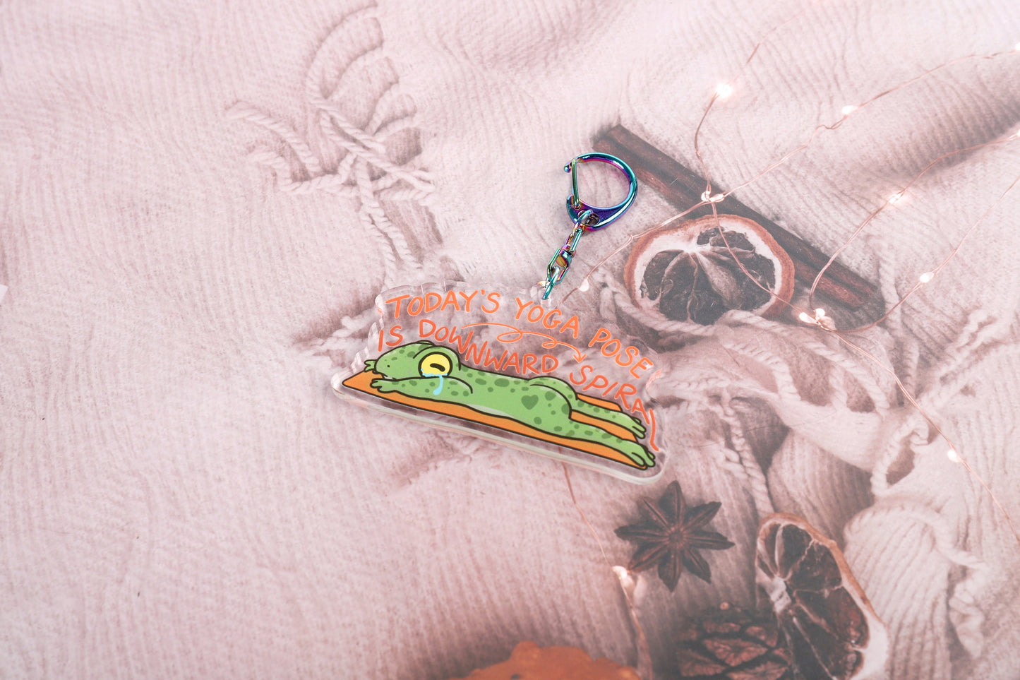 A clear acrylic keyring with a crying frog on a yoga mat, with the words today's yoga pose is downward spiral, in curling font above it. Attached to a blue iridescent claw clasp.