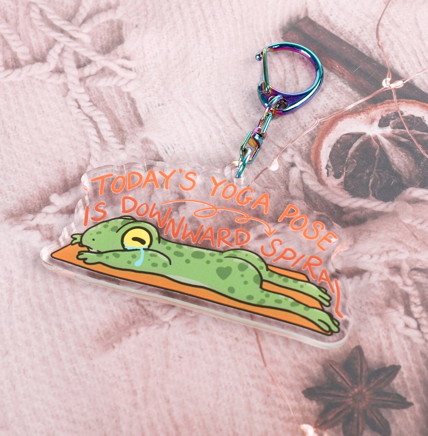 A clear acrylic keyring with a crying frog on a yoga mat, with the words today's yoga pose is downward spiral, in curling font above it. Attached to a blue iridescent claw clasp.