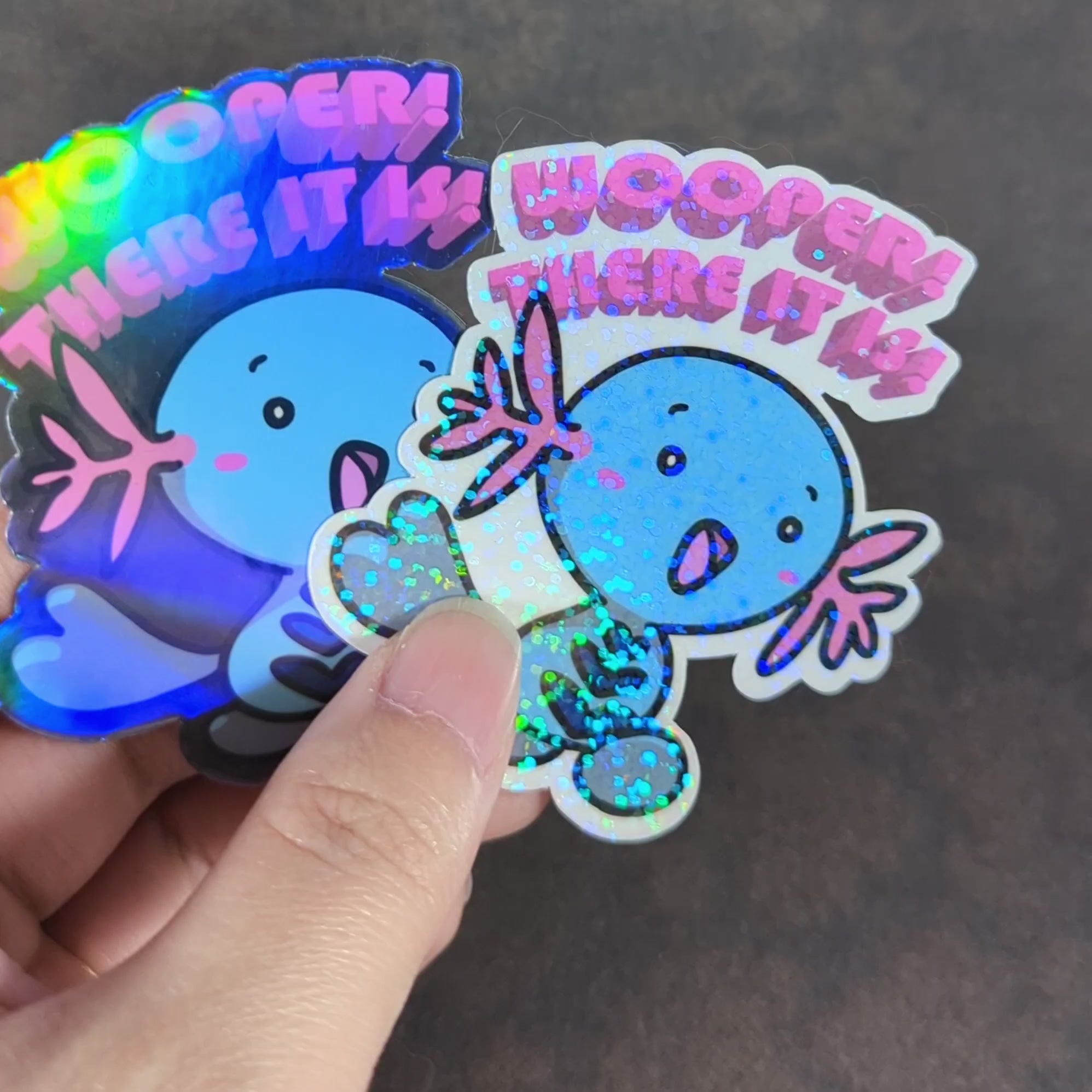 "Video of Holographic 'Wooper! There It Is' stickers featuring a cute blue Wooper from Pokemon, playing off of '90s song hit 'Whoomp! (There It Is)." Perfect for fans of gaming and collectibles. Great for decorating laptops, water bottles, and more."