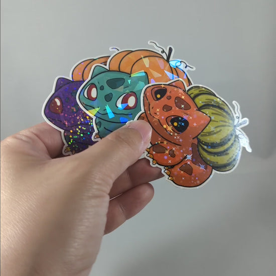 "Video of a cute, Halloween-themed Bulbasaur sticker with holographic effects and a jack-o'-lantern pumpkin on its back. Perfect for Pokemon fans looking for festive, collectible decor with added sparkle."