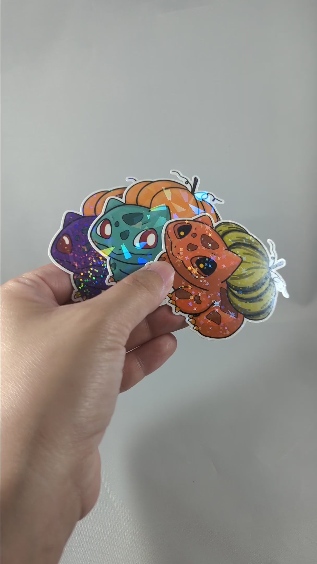 "Video of a cute, Halloween-themed Bulbasaur sticker with holographic effects and a jack-o'-lantern pumpkin on its back. Perfect for Pokemon fans looking for festive, collectible decor with added sparkle."