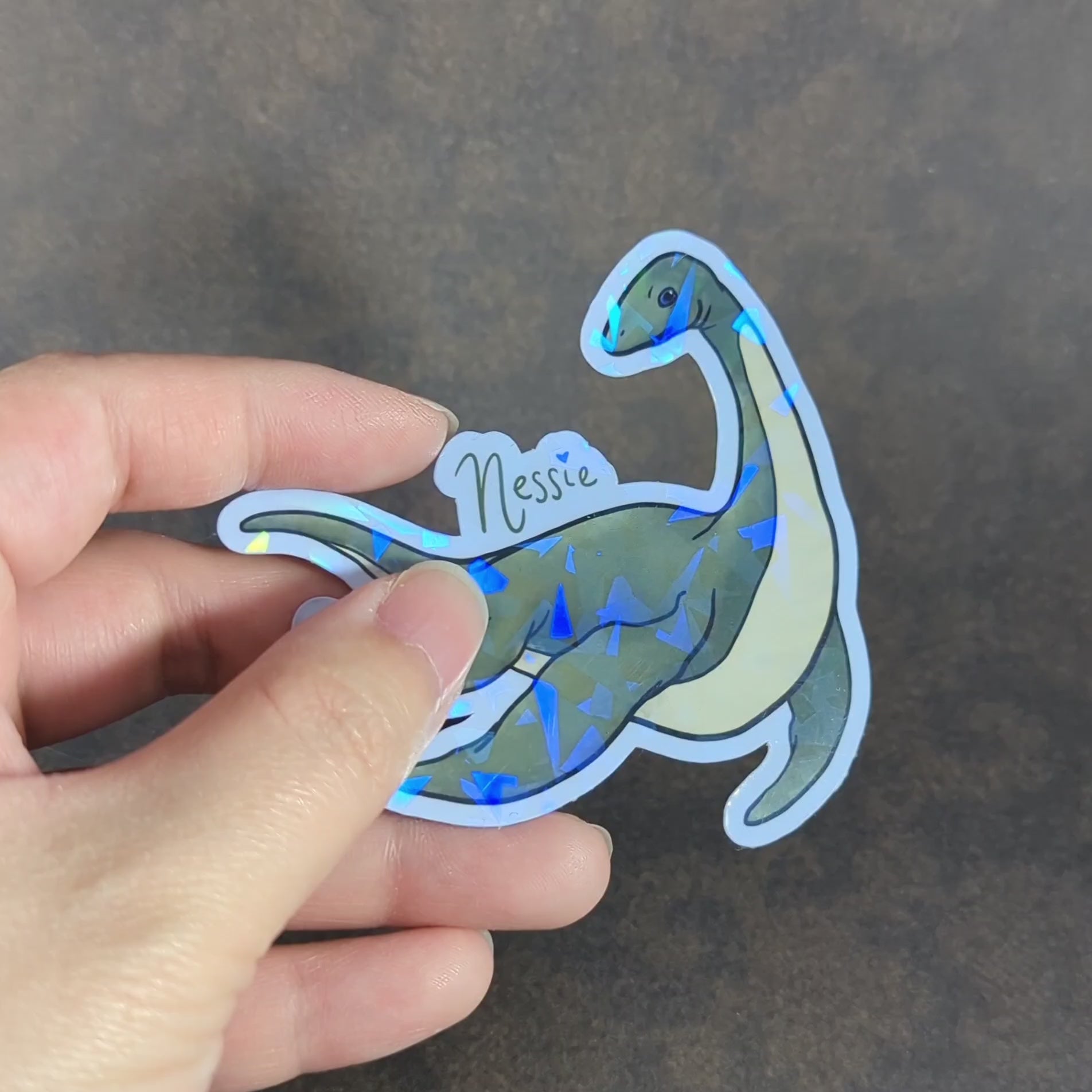 "Video of a holographic Nessie sticker showcasing the Loch Ness Monster with sparkling accents. Ideal for cryptid fans and collectors seeking unique, mythical decor with an eye-catching, supernatural theme."