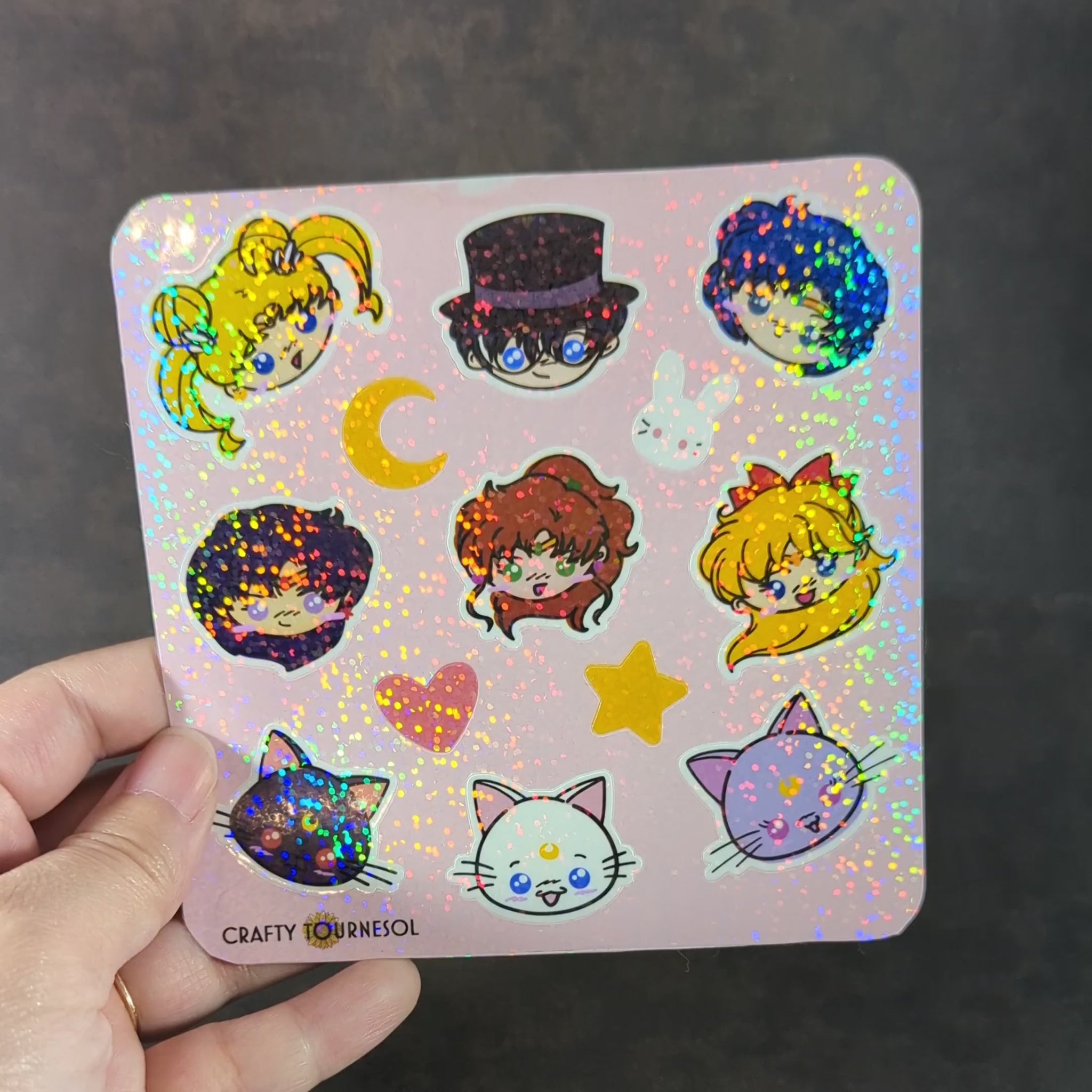 "Video of Holographic sticker sheet featuring chibi characters inspired by Sailor Moon anime series, including moon-themed icons, cute cats, hearts, and stars. Perfect for decorating notebooks, laptops, and more."