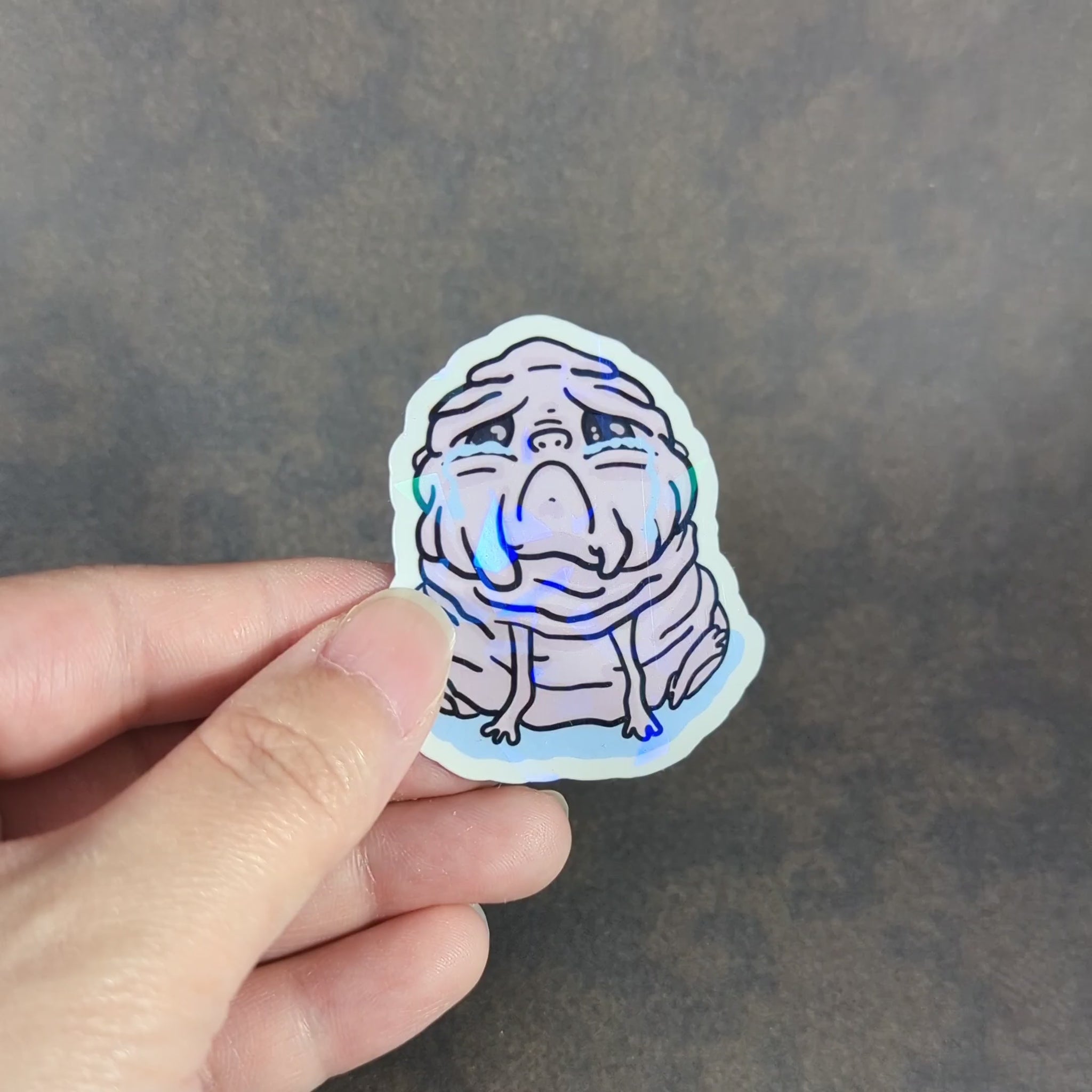 "Video of Squonk stickers featuring the sad, mythical creature in both holographic and matte styles. Ideal for cryptid fans and collectors of unique, emotional supernatural-themed decor."