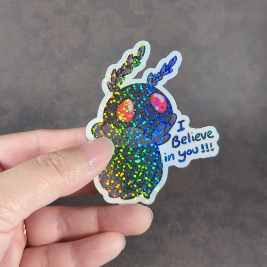 "Video showcasing two Mothman stickers with 'I Believe in You' text, one holographic and one matte. Perfect for cryptid fans and collectors looking for cute, motivational, supernatural-themed decor."